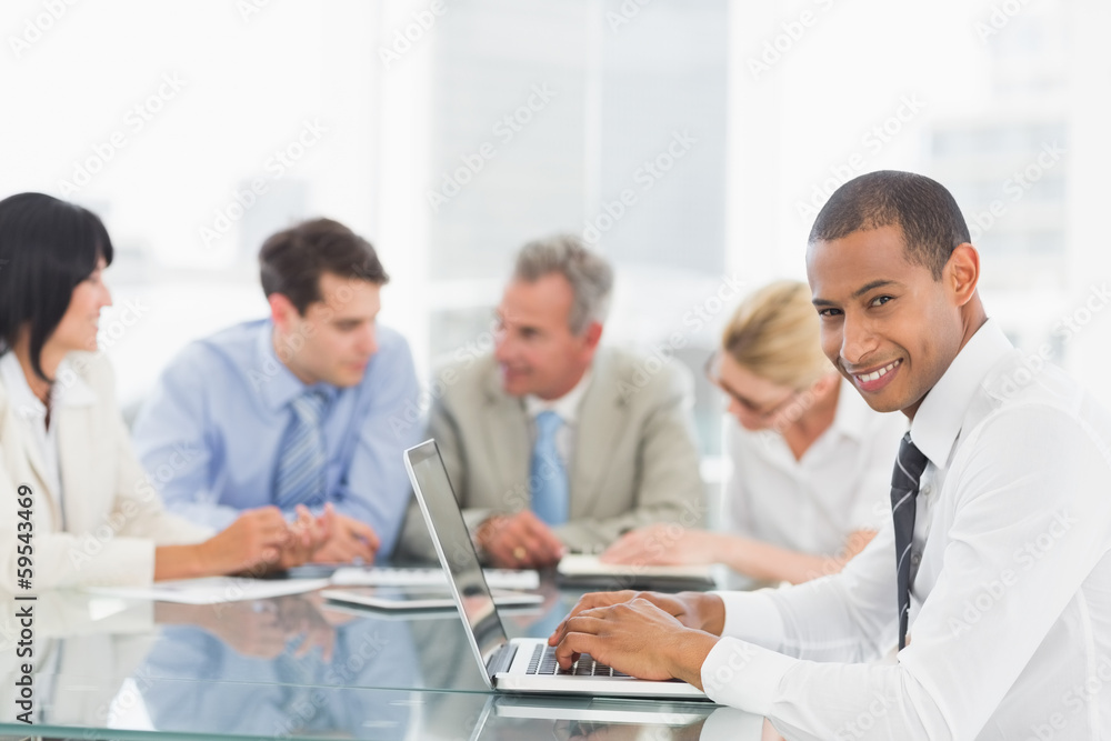 Businessman using laptop during a meeting smiling at camera