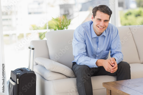 Smiling businessman sitting on couch waiting to leave on busines
