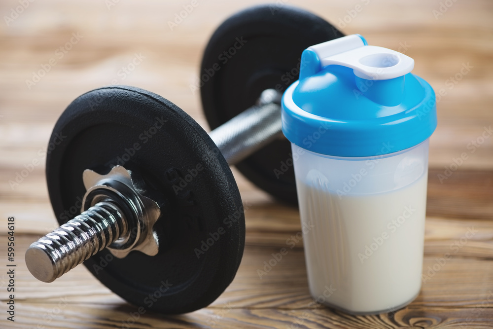 Close-up of a dumbbell and a protein shake on a wooden surface Close-up of a dumbbell and a protein shake on a wooden surface