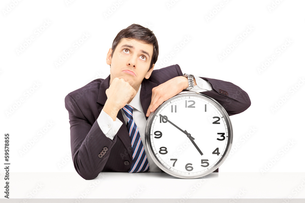 Young businessman deep in thoughts with a clock on a table Young businessman deep in thoughts with a clock on a table