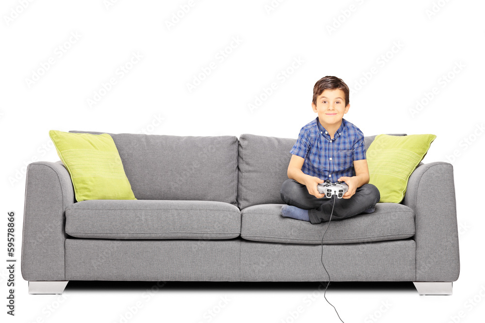 Young smiling kid seated on a sofa playing video games