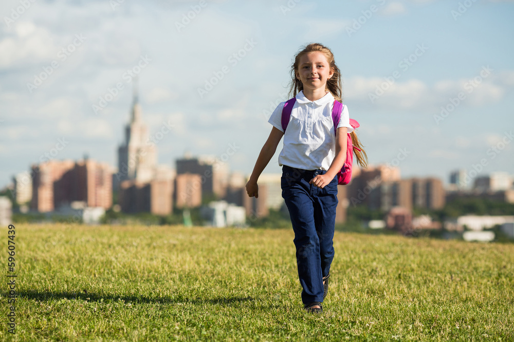 Girl with a backpack walks on grass against urban landscape Girl with a backpack walks on grass against urban landscape
