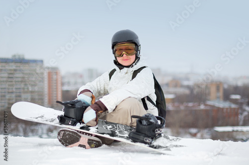 Smiling girl snowboarder in helmet sitting with snowboard photo