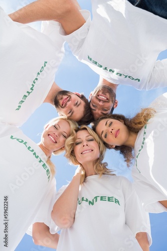 Happy volunteers forming a huddle against blue sky