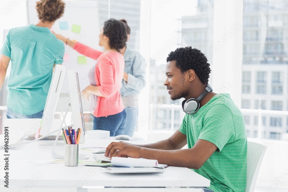 Casual man using computer with group of colleagues behind in off Casual man using computer with group of colleagues behind in off