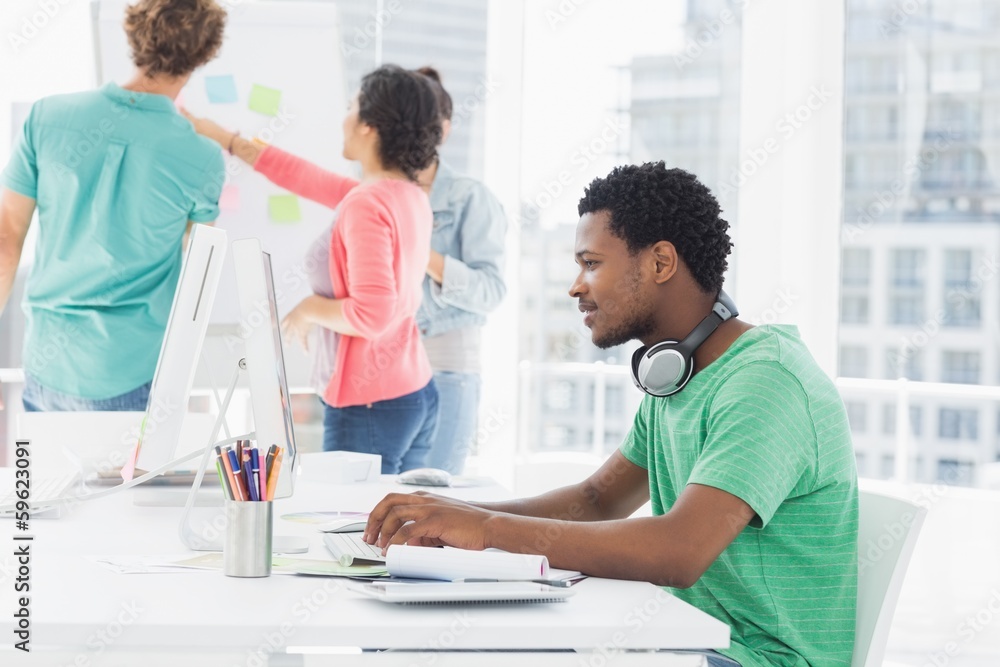 Casual man using computer with group of colleagues behind in off