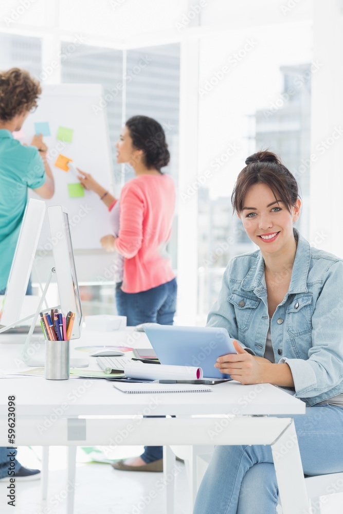 Casual woman using digital tablet with colleagues behind in offi Casual woman using digital tablet with colleagues behind in offi