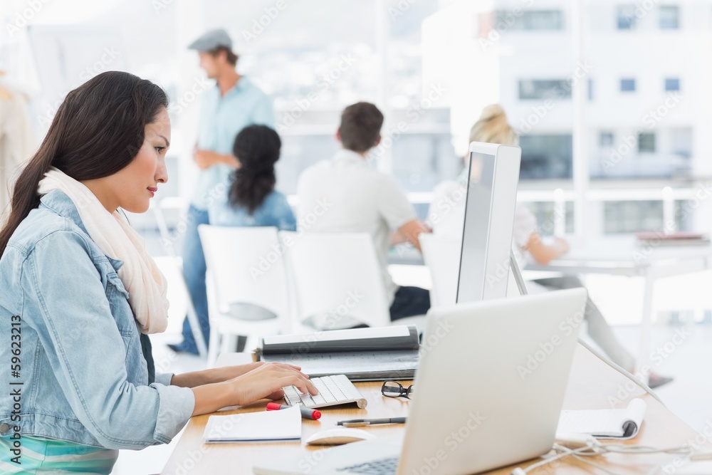 Woman using computer with colleagues behind in office Woman using computer with colleagues behind in office