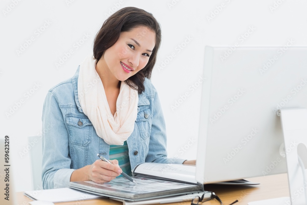 Smiling casual woman with catalog in front of computer in office Smiling casual woman with catalog in front of computer in office