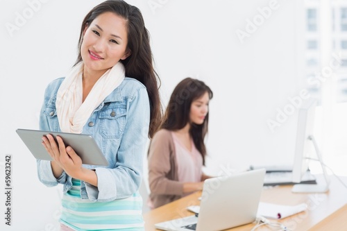 Casual female artist using digital tablet with colleague in back