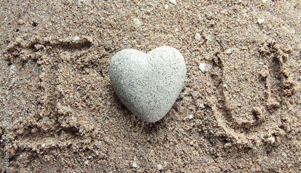 Obraz premium Grey stone in shape of heart, on sand background