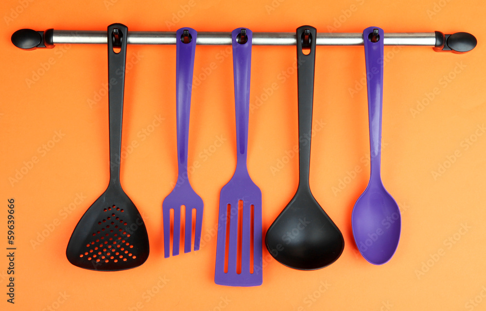 Plastic kitchen utensils on silver hooks on orange background Plastic kitchen utensils on silver hooks on orange background
