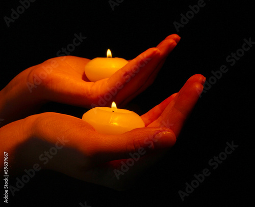 Burning candles in hands isolated on black