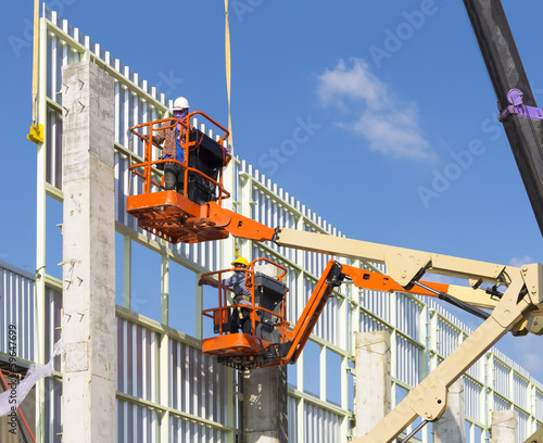 Worker to installation metal sheet on steel structure or frame for wall of facetory, warehouse or industrial building by boom lift or cherry picker and mobile crane for construction at height level.