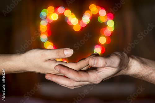 Women's hands in the men's hands holding a heart shaped bokeh