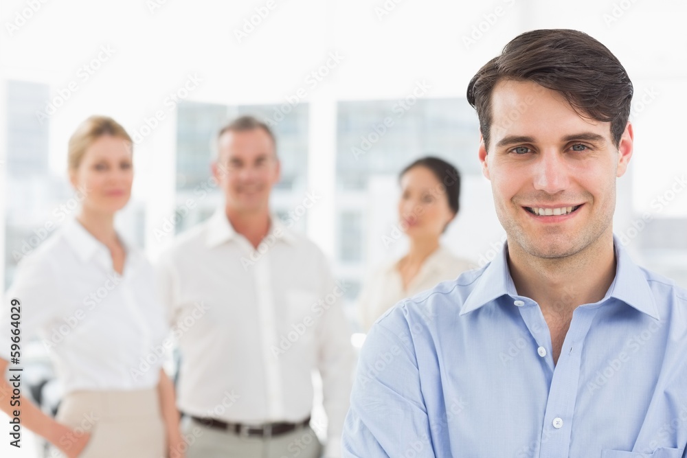 Smiling businessman standing with team behind him Smiling businessman standing with team behind him