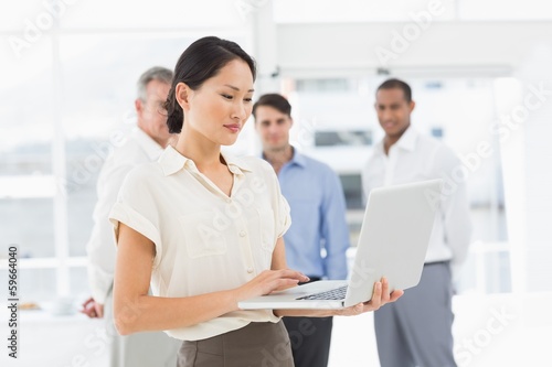 Pretty asian businesswoman using laptop with team behind her