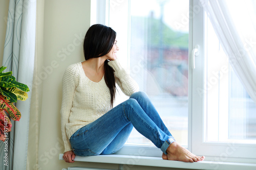 Young happy woman sitting on a window-sill and looking outside