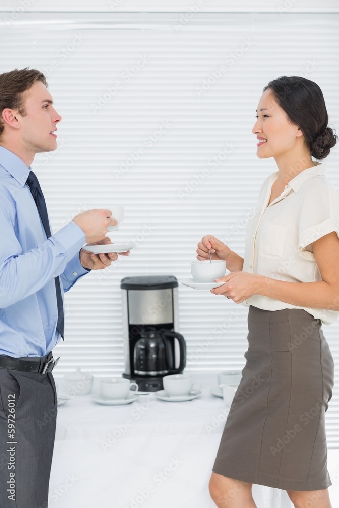 Business couple with tea cups chatting in office Business couple with tea cups chatting in office