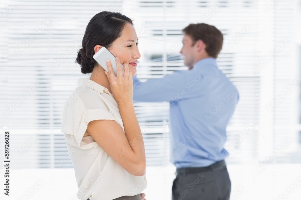Businesswoman using cellphone with man behind at office Businesswoman using cellphone with man behind at office