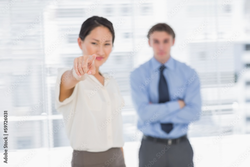 Businesswoman pointing towards camera with man in office Businesswoman pointing towards camera with man in office