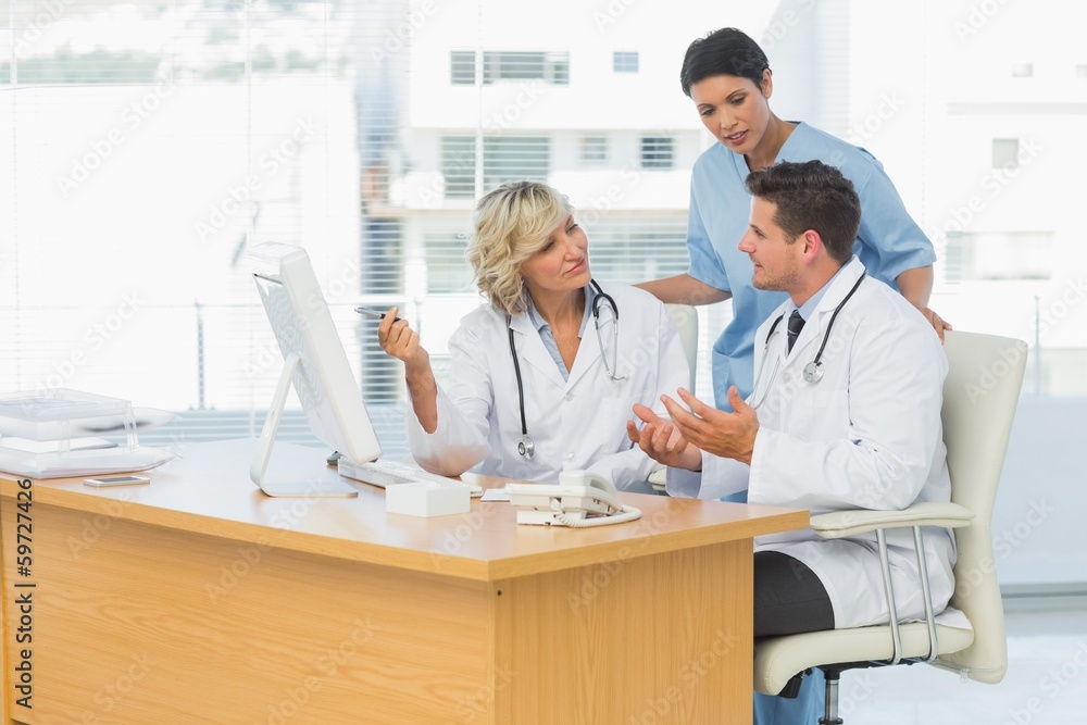 Three concentrated doctors using computer together Three concentrated doctors using computer together
