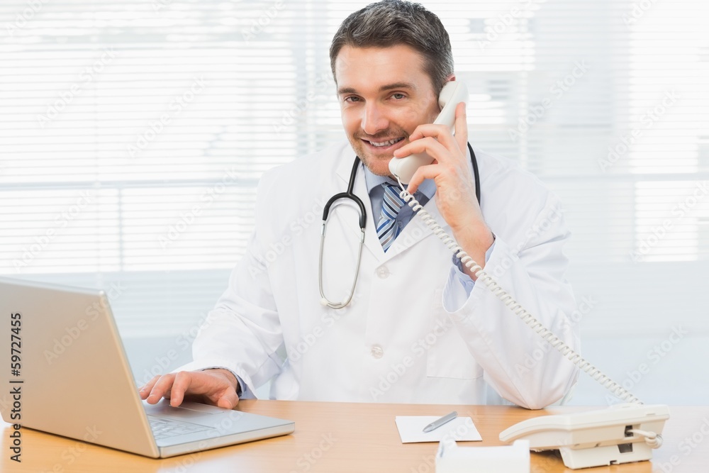 Male doctor using laptop and phone in medical office Male doctor using laptop and phone in medical office