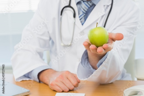 Mid section of a male doctor holding an apple