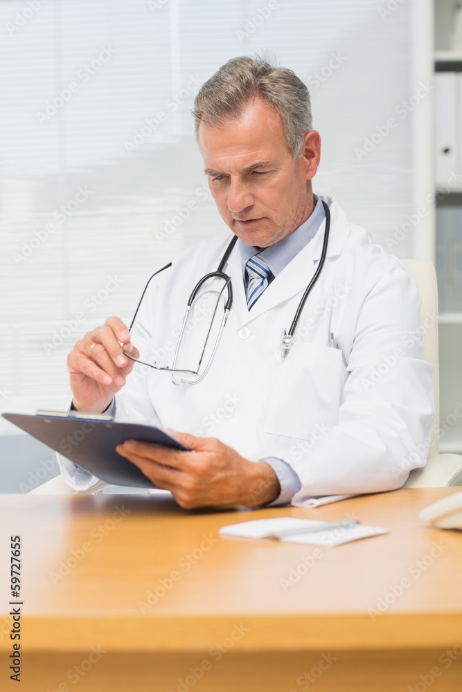 Concentrating mature doctor sitting at his desk with clipboard