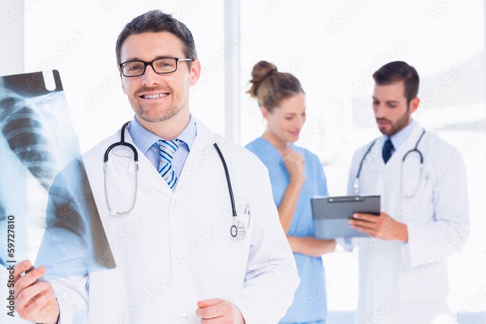 Male doctor examining x-ray with colleagues behind Male doctor examining x-ray with colleagues behind