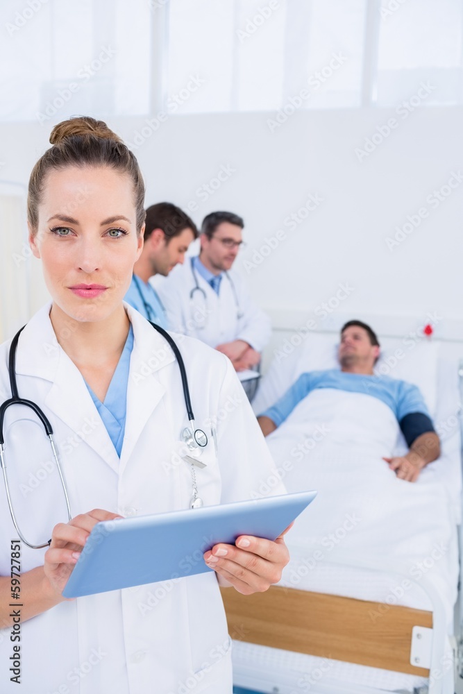 Doctor using digital tablet with colleagues and patient behind Doctor using digital tablet with colleagues and patient behind
