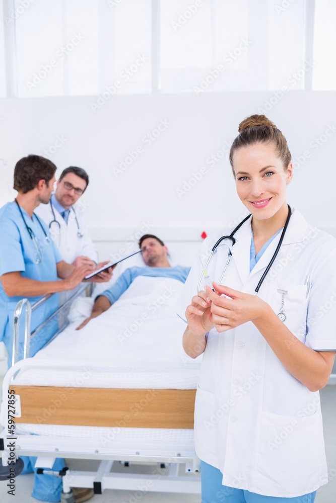 Doctor holding syringe with colleagues and patient in hospital Doctor holding syringe with colleagues and patient in hospital