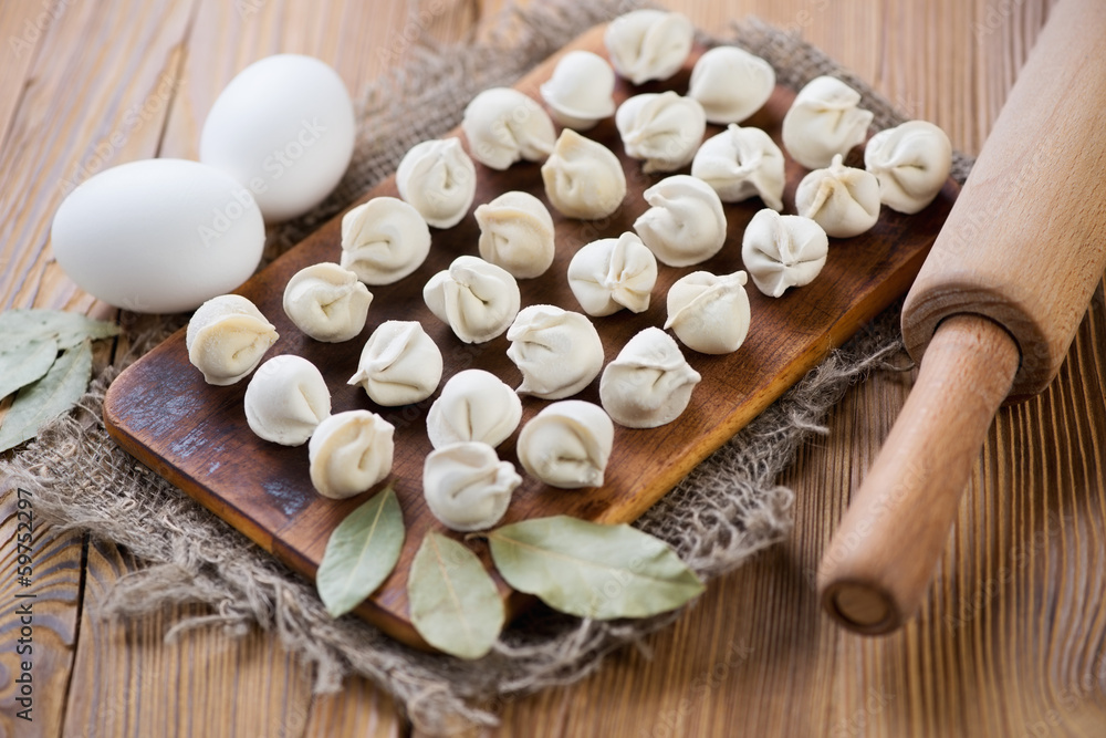 Raw pelmeni, eggs, bay leaves and rolling pin on a wooden table Raw pelmeni, eggs, bay leaves and rolling pin on a wooden table
