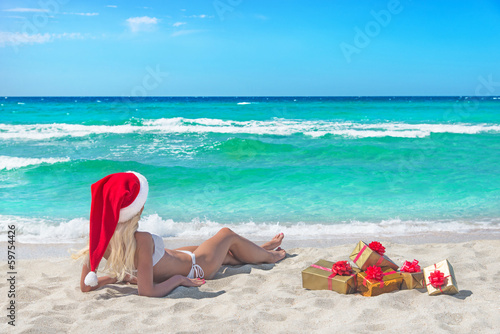 Beautiful blonde woman in bikini, red christmas hat and gift box