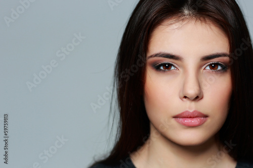 Closeup portrait of a young mysterious woman on gray background