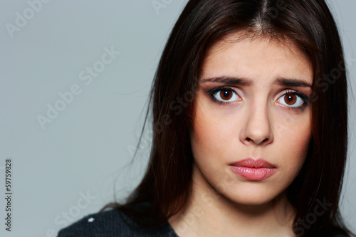 Closeup portrait of a young sad woman on gray background