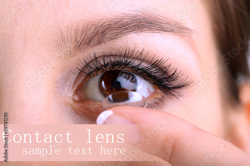 Young woman putting contact lens in her eye close up