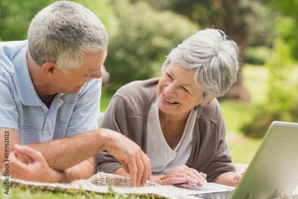 Smiling senior couple using laptop at park Smiling senior couple using laptop at park