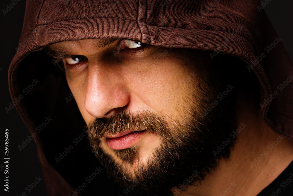 Close-up portrait of threatening man with beard wearing a hood