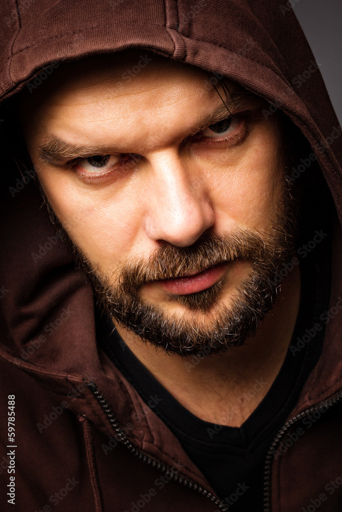 Close-up portrait of threatening man with beard wearing a hood