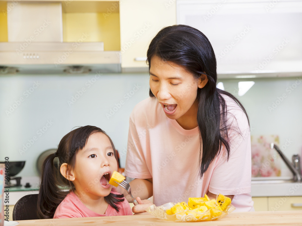 Mother feeding daughter eating fruits in the kitchen
