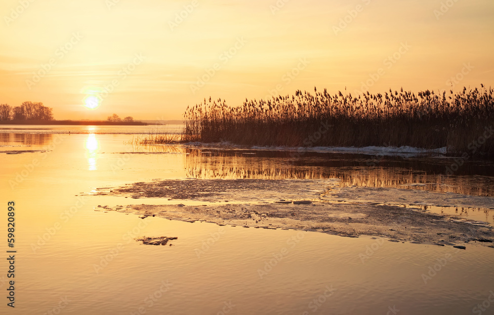 Winter landscape with river and sunset fiery sky.