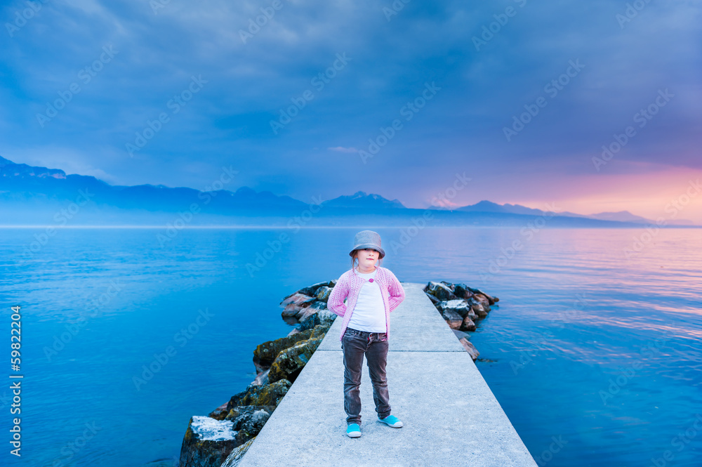 Portrait of a cute little girl on sunset standing on a pier
