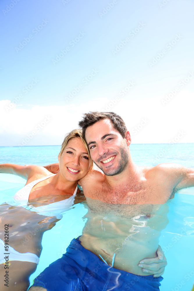 Cheerful couple swimming in infinity pool Cheerful couple swimming in infinity pool