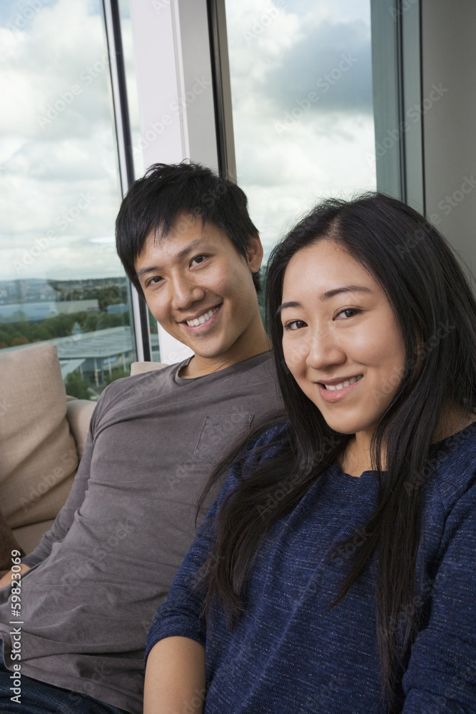 Portrait of happy Asian couple sitting on sofa at home Portrait of happy Asian couple sitting on sofa at home