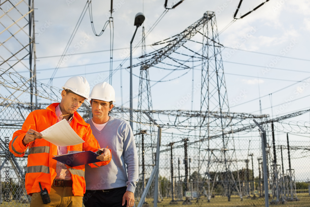 Male architects reviewing documents together at electric power plant Male architects reviewing documents together at electric power plant