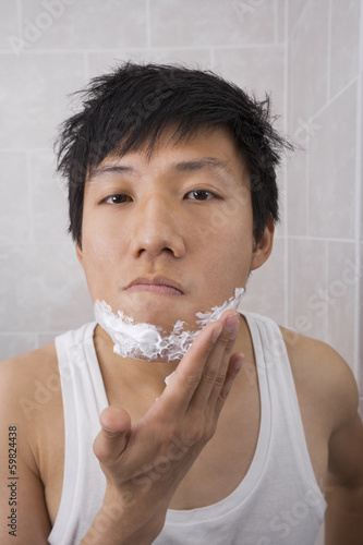Portrait of mid adult man applying shaving foam on face in bathroom