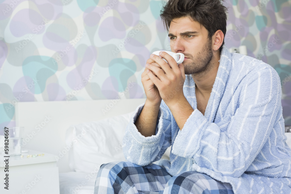 Sick man drinking coffee while sitting on bed at home Sick man drinking coffee while sitting on bed at home