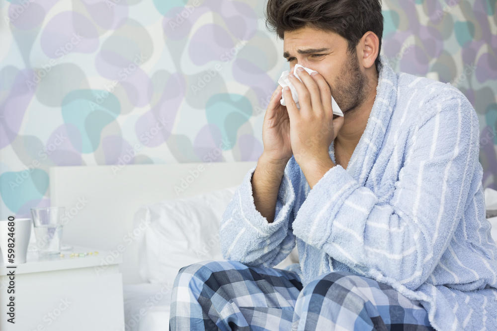 Sick man blowing his nose in tissue paper on bed at home Sick man blowing his nose in tissue paper on bed at home
