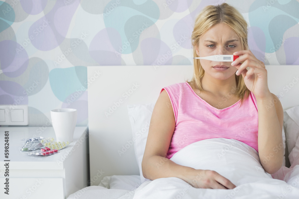 Sick young woman taking temperature with thermometer in bed Sick young woman taking temperature with thermometer in bed